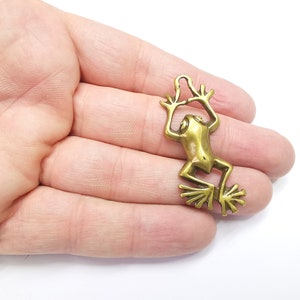 May include: A gold-colored metal frog charm with a loop at the top for attaching to a necklace or bracelet.