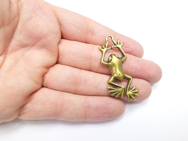 May include: A gold-colored metal frog charm with a loop at the top for attaching to a necklace or bracelet.