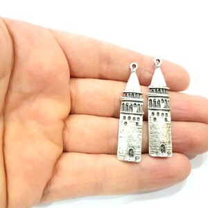 Puede incluir: Dos colgantes de plata con forma de minarete con detalles intrincados. Los colgantes est&aacute;n sobre un fondo blanco.