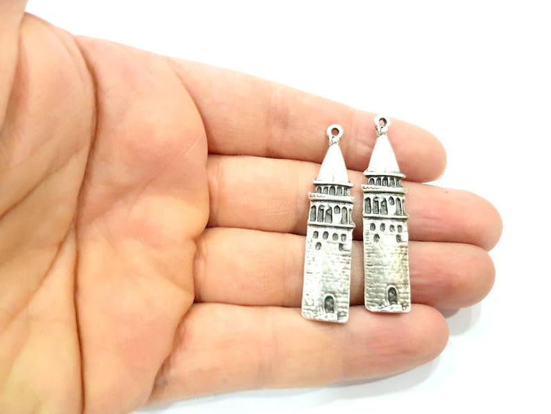 Puede incluir: Dos colgantes de plata con forma de minarete con detalles intrincados. Los colgantes est&aacute;n sobre un fondo blanco.