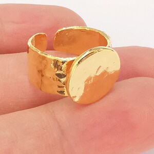 May include: A gold-toned ring with a hammered band and a large, round, smooth disc on top.