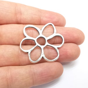 以下が含まれることがあります： 6枚の花びらを持つ花の形をした銀色の金属製のチャーム。チャームはハンマード加工が施されており、中央が開いています。