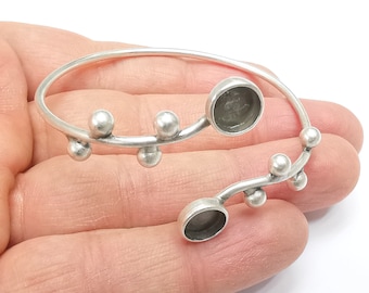 May include: Silver bangle bracelet with a unique design featuring a series of small spheres and two open circles. The bracelet is open and adjustable.