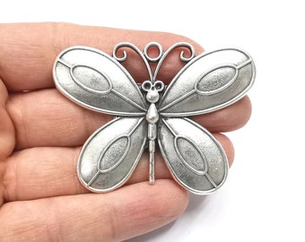Puede incluir: Encanto de mariposa de metal plateado con detalles intrincados y un acabado texturizado. La mariposa tiene un diseño delicado con alas curvas y una cabeza pequeña.