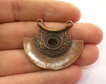 May include: A copper-colored metal pendant with a circular design and a hole in the center. The pendant has a textured surface and two loops at the top for attaching a chain.