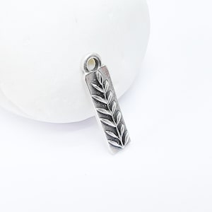 May include: Silver charm with a detailed leaf design. The charm is rectangular and has a loop at the top for attaching to a necklace or bracelet.