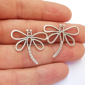 May include: Two silver dragonfly charms with intricate details. The charms are openwork and have a delicate, airy design.