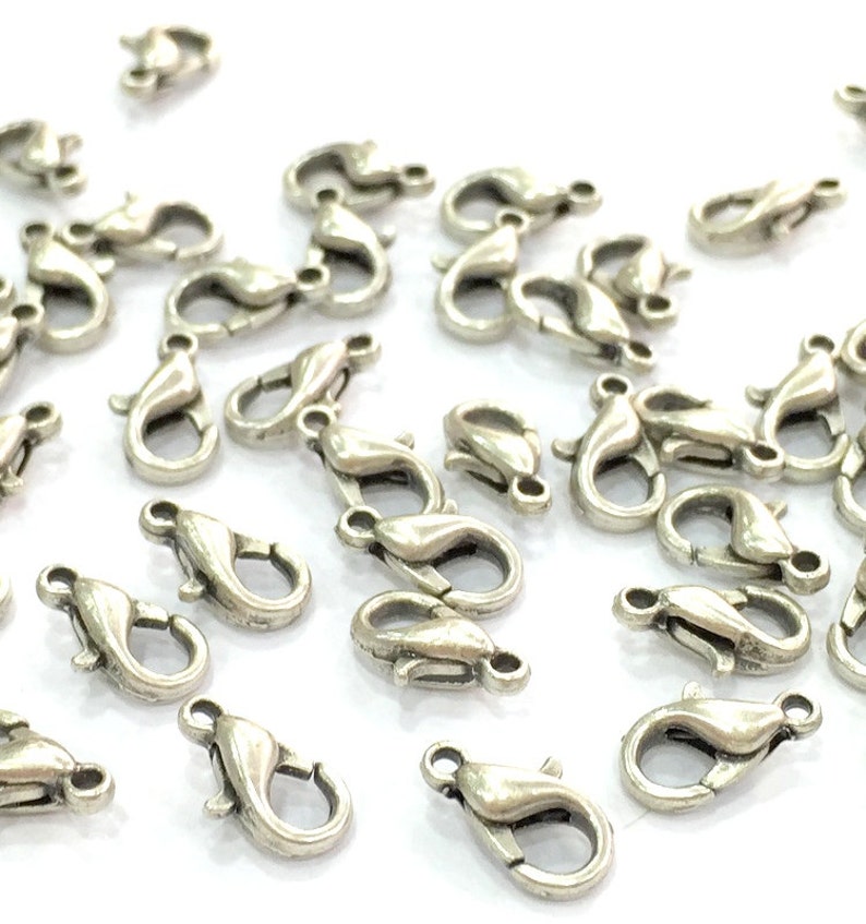 May include: A group of silver-toned lobster clasps, a type of jewellery finding used for attaching chains or cords to jewellery pieces.
