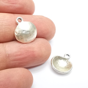 May include: Two silver metal charms in the shape of a circle and a half-circle. The charms have a hammered texture and a loop for attaching to a chain or bracelet.