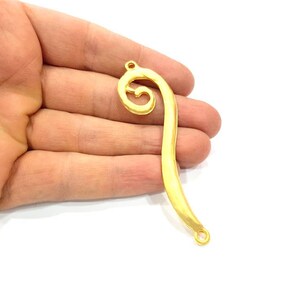 May include: Gold-toned metal pendant with a decorative swirl design and two jump rings.