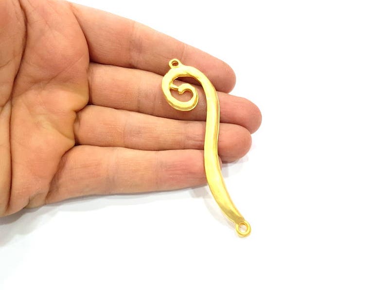 May include: Gold-toned metal pendant with a decorative swirl design and two jump rings.