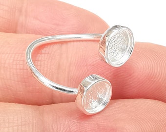 Puede incluir: Anillo de plata con dos engastes redondos de fondo abierto. Los engastes están unidos a la banda del anillo con una barra curva.