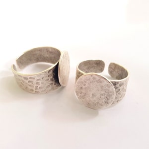 May include: Two silver rings with a round, flat, silver surface on top. The rings are textured with a hammered finish.