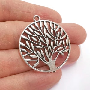 May include: Silver-toned metal pendant featuring a tree of life design. The pendant is circular and has a detailed, intricate design of a tree with branches and leaves.