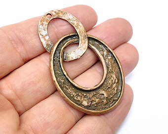 May include: A copper-toned metal pendant with a textured, hammered finish. The pendant features two interlocking oval shapes, one slightly larger than the other.