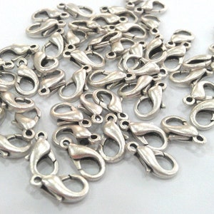 May include: A pile of silver-toned lobster clasps, a type of fastener used for jewelry making.