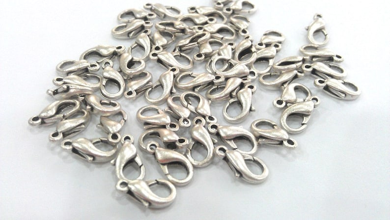 May include: A pile of silver-toned lobster clasps, a type of fastener used for jewelry making.