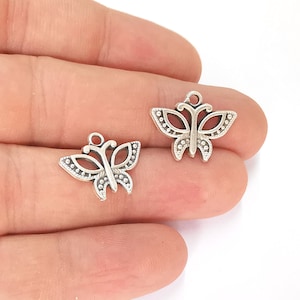 Op de afbeelding: Twee zilveren vlinderbedels met ingewikkelde details. De bedels hebben een lus aan de bovenkant om aan sieraden of andere knutselwerkjes te bevestigen.
