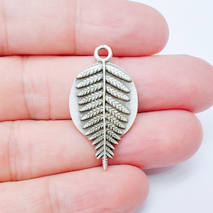 May include: A silver-colored fern leaf charm with a loop at the top for jewelry making. The charm features detailed leaf veins and a textured surface, perfect for pendants or earrings.