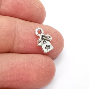 May include: Silver charm in the shape of a small house with a star on the front. The charm has a loop at the top for attaching to a bracelet or necklace.
