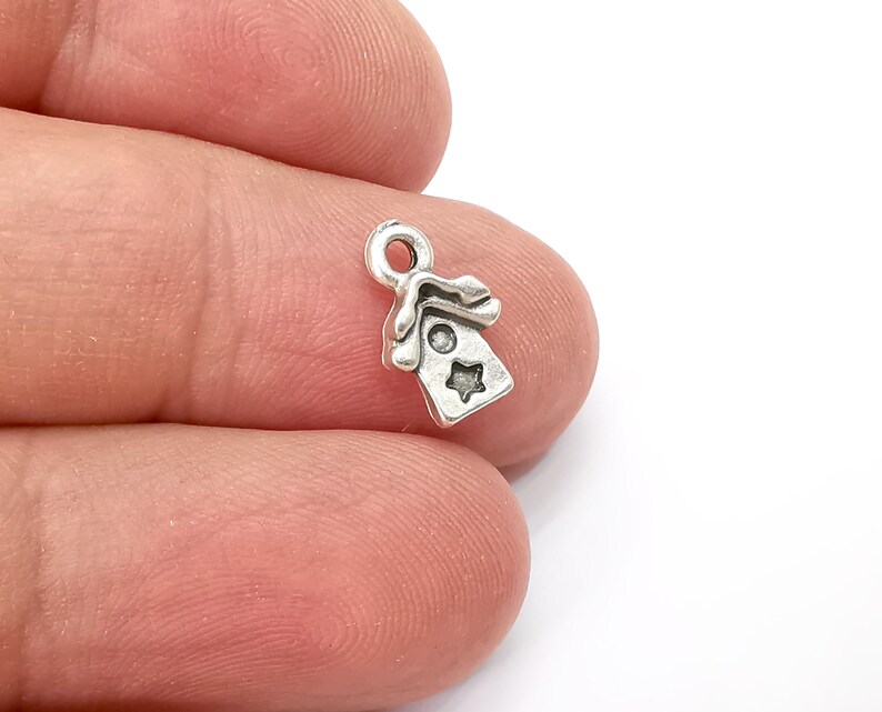 May include: Silver charm in the shape of a small house with a star on the front. The charm has a loop at the top for attaching to a bracelet or necklace.
