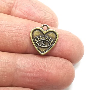 Könnte beinhalten: Ein bronzefarbener Anhänger in Herzform mit einem bösen Auge im Inneren. Der Anhänger hat oben eine Öse zum Anbringen an einer Halskette oder einem Armband.