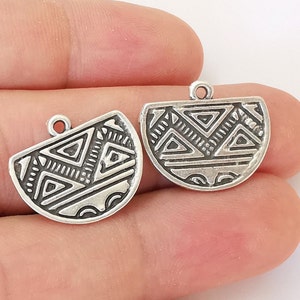 May include: Two silver-toned metal charms with a geometric pattern. The charms are shaped like half circles and have a loop at the top for attaching to a necklace or bracelet.