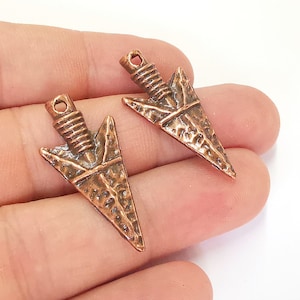 May include: Two copper arrowhead charms with a textured surface. The arrowheads have a loop at the top for attaching to jewelry or other crafts.