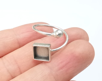 May include: Silver ring with a square bezel setting. The ring is adjustable and has a small ball at the top.