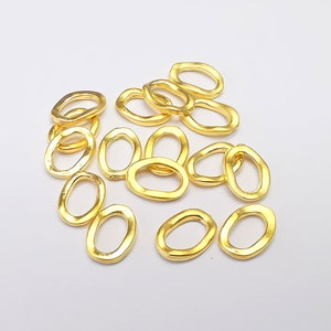 May include: A group of 15 gold-colored oval jump rings. The rings are all the same size and have a slightly irregular shape.