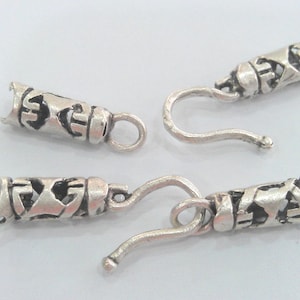 Pode incluir: Quatro tampas de extremidade de metal prateadas com um design decorativo e um gancho. As tampas de extremidade medem aproximadamente 2,5 cm de comprimento.