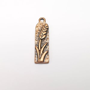 May include: A gold-toned metal charm with a wheat stalk design. The charm has a textured surface and a loop at the top for attaching to a necklace or bracelet.