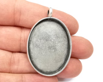 May include: Silver pendant tray with a round, smooth, and slightly textured surface. The tray is designed for resin crafting and has a loop at the top for attaching a chain.