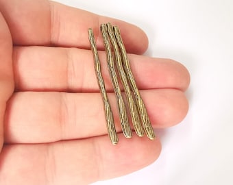May include: Close-up of several textured, gold-colored metal stick-shaped jewelry findings. The findings have a rough, organic appearance, resembling small branches or twigs. They are arranged in a hand against a white background.