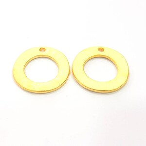 May include: Two gold-colored metal rings with a small hole at the top. The rings are smooth and have a slightly textured surface.