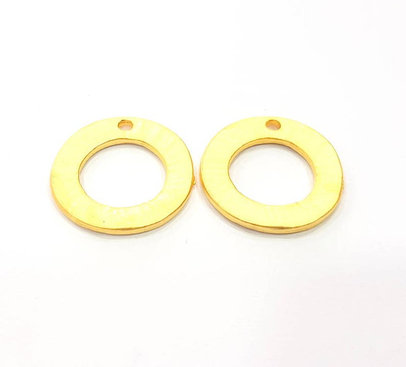 May include: Two gold-colored metal rings with a small hole at the top. The rings are smooth and have a slightly textured surface.