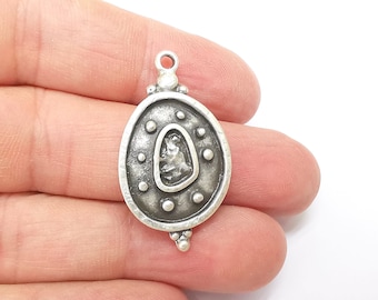 May include: Silver oval pendant with a raised design of a figure inside a circle surrounded by dots. The pendant has a loop at the top for attaching a chain.