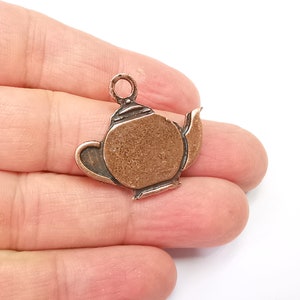 May include: A copper-colored teapot charm with a loop for hanging. The charm has a textured surface and a detailed design.