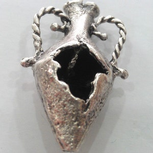 May include: Silver pendant in the shape of a broken, ornate vase with a rope-like design around the top.