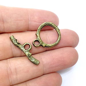 May include: Two antique gold metal toggle clasps in a twig design. The clasp on the left is a straight bar with a hole on each end. The clasp on the right is a circle with a hole on the side.
