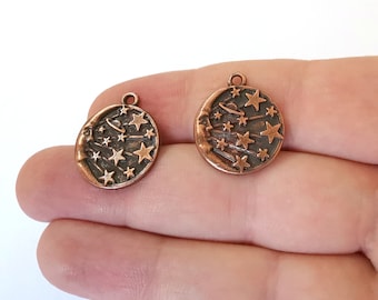 May include: Two copper-toned metal charms with a crescent moon and stars design. The charms are round and have a hole at the top for attaching to a necklace or bracelet.
