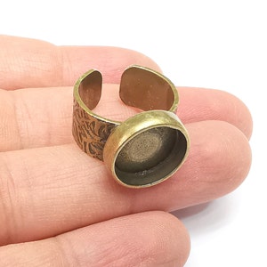 May include: A gold-toned adjustable ring with a round bezel setting. The ring is decorated with a floral pattern.