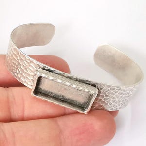 May include: Silver cuff bracelet with a rectangular bezel for a cameo or other embellishment. The bracelet has a hammered texture.