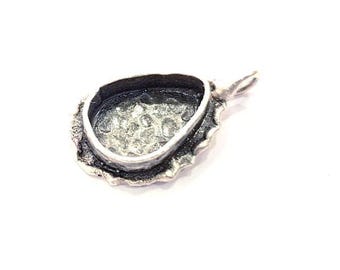 May include: Silver pendant setting with a scalloped edge and a teardrop-shaped bezel. The bezel is open on the back, ready to be filled with a stone or other material.