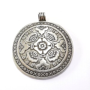 May include: A silver-colored, round pendant with an intricate floral design. The pendant features a central flower surrounded by stylized leaves and a dotted border. It has a loop at the top for a chain.
