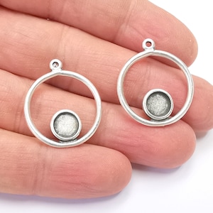 May include: Two silver-coloured round pendant settings with a small circular base. Each setting has a loop at the top for attaching to a chain or cord. The settings are designed for jewellery making.