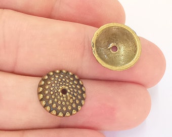 Può includere: Due perline in metallo color ottone antico. Una perlina è un piccolo disco piatto con una superficie strutturata di piccoli punti in rilievo. L'altra perlina è un piccolo cono di metallo color ottone con un foro al centro.