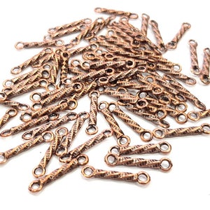 Op de afbeelding: Een stapel koperkleurige metalen connectorstukken met een gedraaid ontwerp. Elk stuk heeft twee lussen aan de uiteinden.