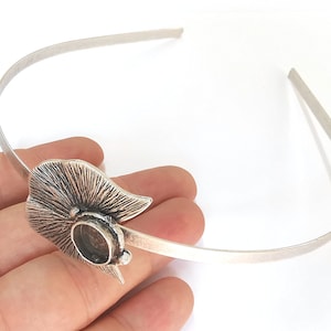 May include: Silver headband with a leaf-shaped design and a round, textured detail.
