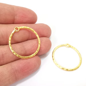 May include: Two gold-toned hammered metal hoops with a jump ring opening. The hoops are approximately 1 inch in diameter.
